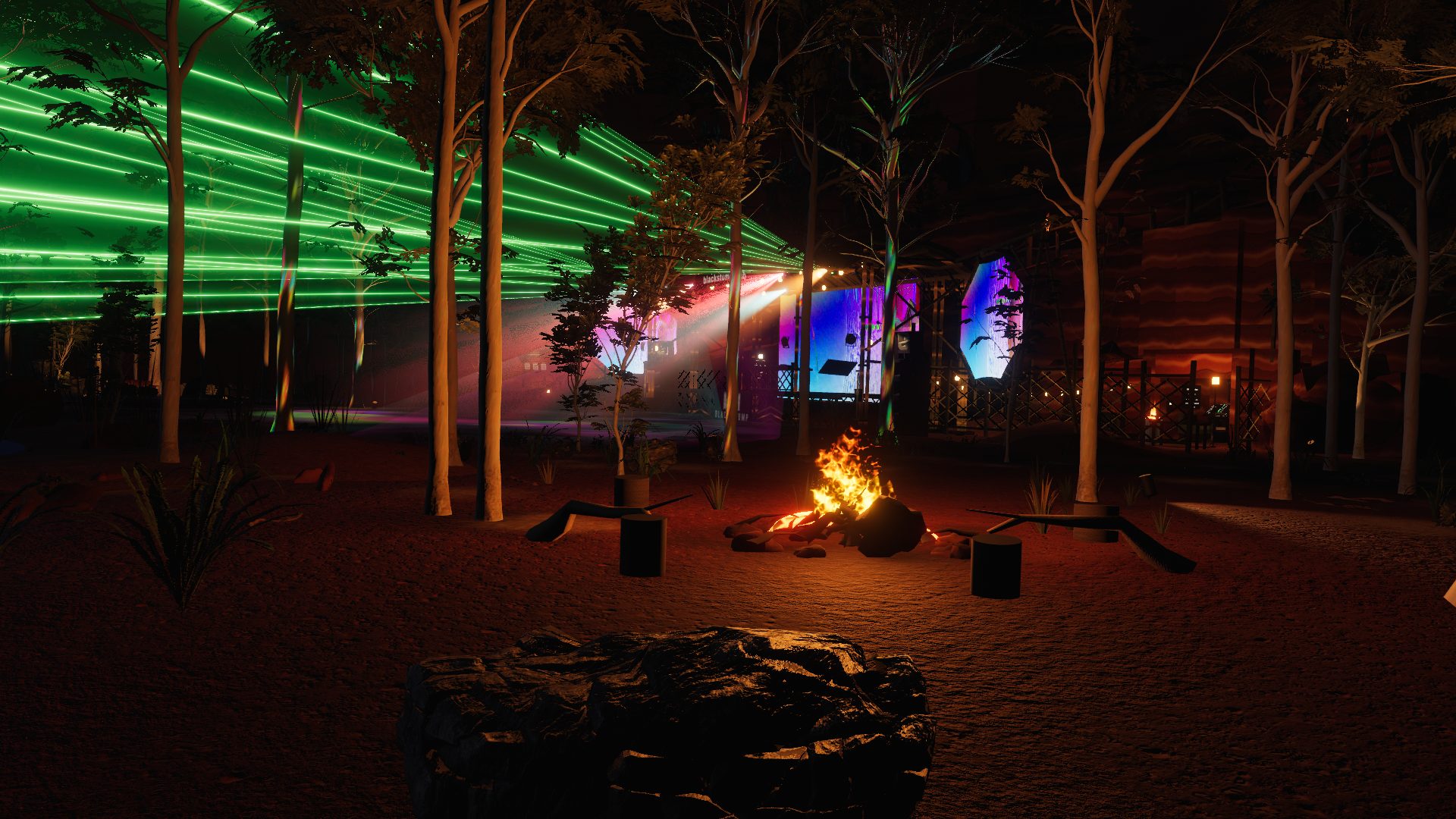 The campfire in the red dirt under the gums, with the stage lit up through the trees behind it: green lasers overhead and the VJ screens glowing